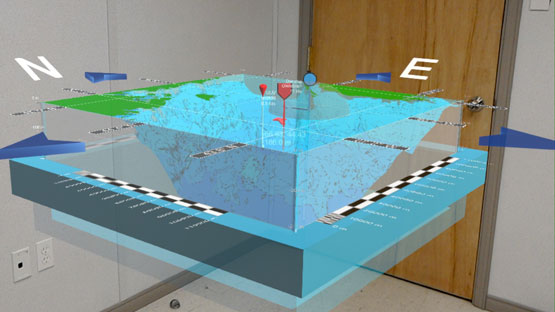 A virtual three-dimensional model, showing the ocean and coastline, appears to float in the corner of a room.