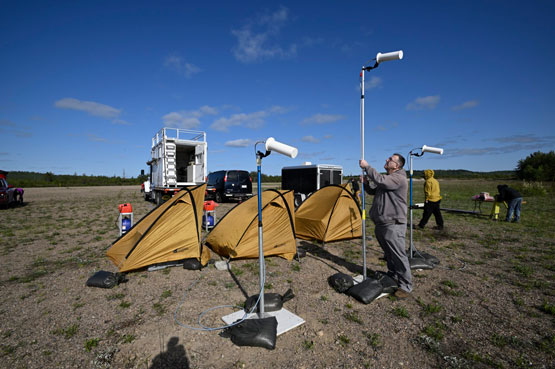 A person setting up white antennas outside beside three yellow tents.
