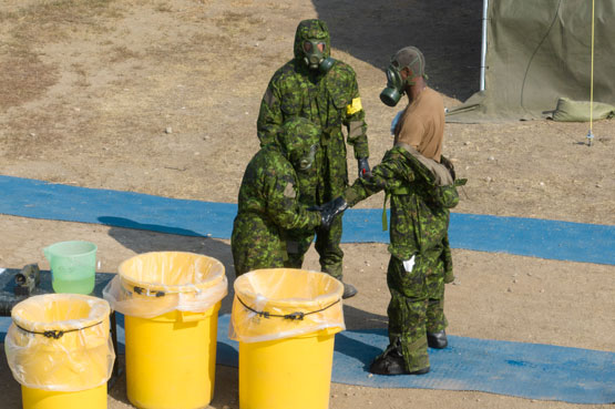 Soldiers in protective gear removing another soldier’s protective gear