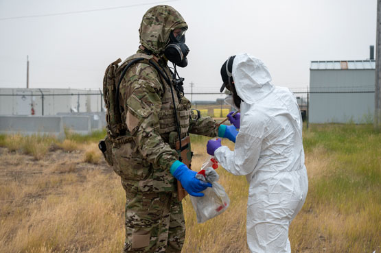 Soldier in camouflage protective gear being swabbed by staff in white protective gear