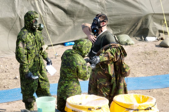 Soldiers in protective gear removing another soldier’s protective gear